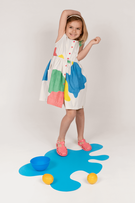 Robe fille légère et structurée. Motif coloré peinture. Boutonnière rose et poche. 100% Coton biologique.